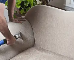 Professional upholstery cleaner deep-cleaning a fabric sofa with a handheld extraction tool and hose in Columbus, GA.